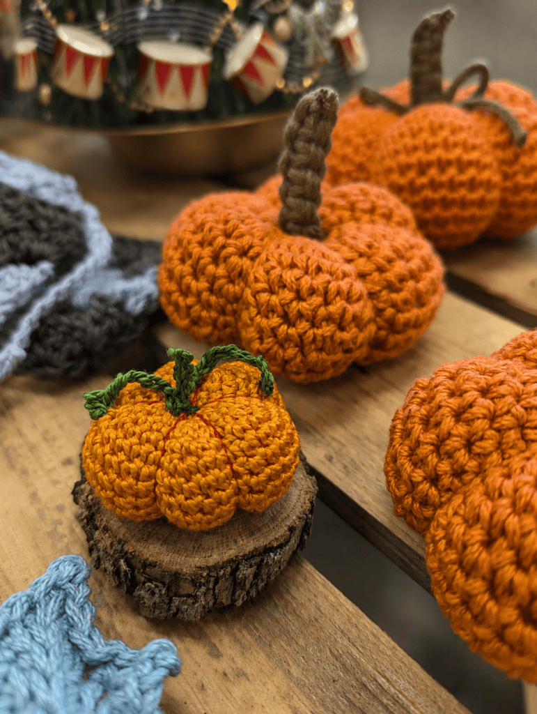 Handmade crocheted pumpkins displayed on wooden shelves and a small wood slice.